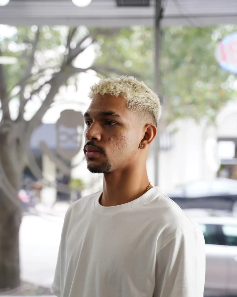 Platinum blonde curls above a clean skin fade, colored and cut by Luis Mosquera